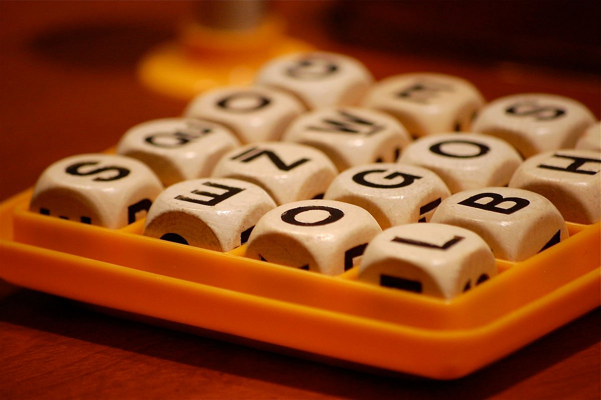 Boggle game setup with letter dice arranged in a grid, timer, and score pad
